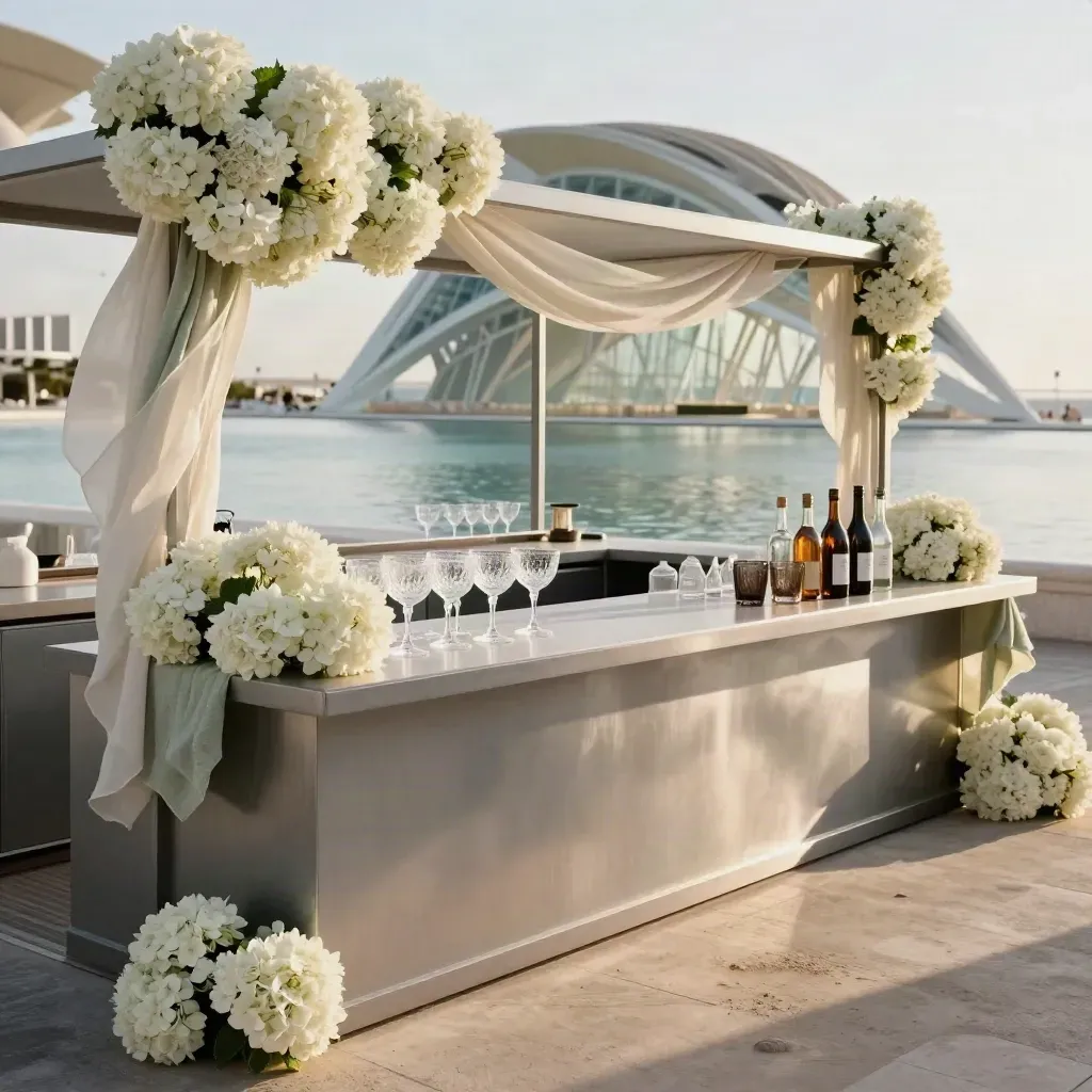 Terraza de cóctel lista para prensa con flores blancas, copas y reflejos de agua.